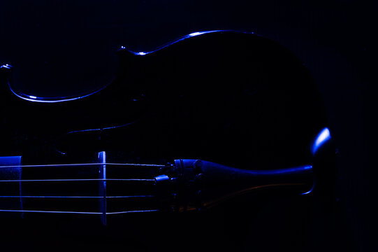 A violin on a dark background, side lit with blue lights