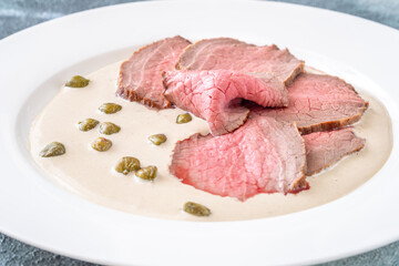 Elegant Vitello Tonnato with scattered capers and creamy sauce on plate