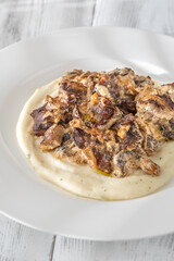 Braised meat and mushroom topping over creamy mashed potato served on white plate