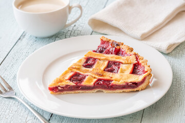Wedge of cherry pie with coffee and fork on bright rustic table