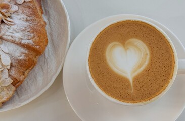 Cup of coffee with heart latte art and almond croissant
