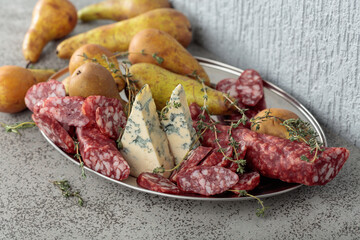 Blue cheese, dry-cured sausages, thyme and pears on a stone table.