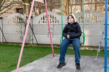 Young boy enjoying a quiet afternoon on a swing set in a backyard during early spring