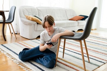 Boy sitting on the floor using smartphone in a cozy living room during the afternoon