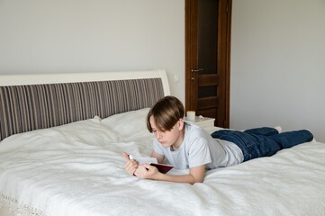 Young boy enjoys a story in the book while lying on a cozy bed in a bright bedroom during daylight hours