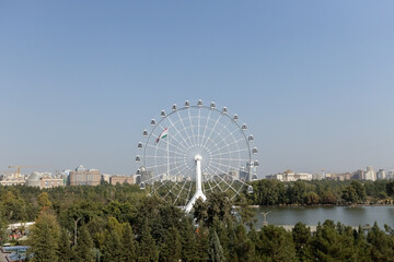 Fototapeta premium Scenic lakeside view of the Navruz Palace and Ferris wheel in Dushanbe, Tajikistan, showcasing the grand architecture and modern attractions under a clear sky