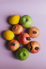 Fresh and colorful still life with ripe pomegranates, lemons, and green apples on a soft purple background. Modern food photography concept for healthy eating, freshness, and organic lifestyle themes 