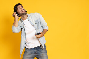 Young man listening favorite music on mobile phone application with wireless headphones and dancing, Top music chart concept