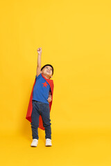 Asian little boy superhero smiling, hand up with red cape isolated yellow background, Full body composition