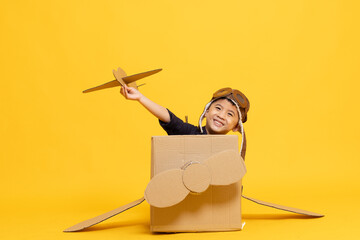 Asian little boy aviator playing with cardboard airplane isolated on yellow background, Kid toy diy concept