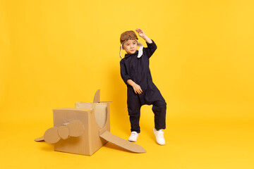 Asian little boy aviator playing with cardboard airplane and dancing isolated on yellow background, Kid toy diy concept