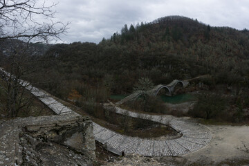 View of the traditional stone Kalogeriko or Plakidas bridge with cobblestone path on a winter day, Zagori, Epirus, Greece