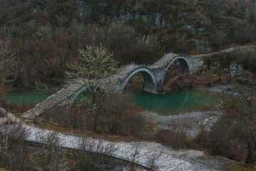 View of the traditional stone Kalogeriko or Plakidas bridge with cobblestone path on a winter day, Zagori, Epirus, Greece