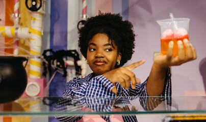 Young Black woman pointing at spooky Halloween drink with funny expression
