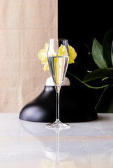 Glasses of water with a reflected yellow orchid. Beige and black background.