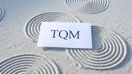 White paper with TQM text placed on a smooth sandy background