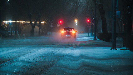 Cars driving along an evening winter city street during a snowstorm
