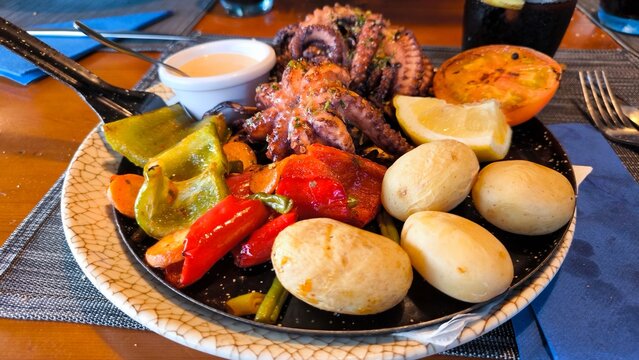 Traditional Canarian dish with grilled octopus, wrinkled potatoes, roasted bell peppers, green and red paprika, lemon slices, mojo sauce. Authentic Canary Islands cuisine served in local restaurant.