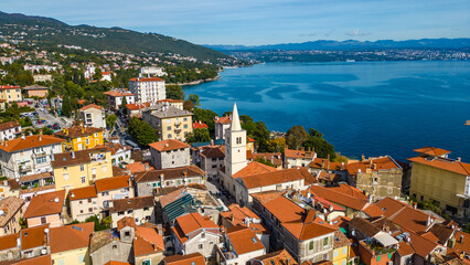 Scenic aerial view of the coastal town Lovran on the Opatija Riviera, Croatia, with red-roofed houses, Adriatic Sea, and green Učka mountain slopes in the background