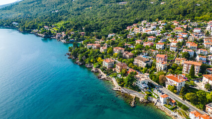 Scenic aerial view of the coastal town Lovran on the Opatija Riviera, Croatia, with red-roofed houses, Adriatic Sea, and green Učka mountain slopes in the background