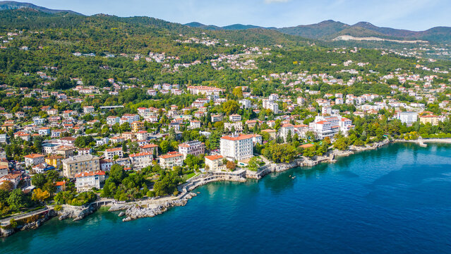 Aerial view of the Hotel Excelsior and the coastal promenade in Lovran, Croatia, surrounded by red-roofed houses, Adriatic Sea, and lush green hills of the Opatija Riviera