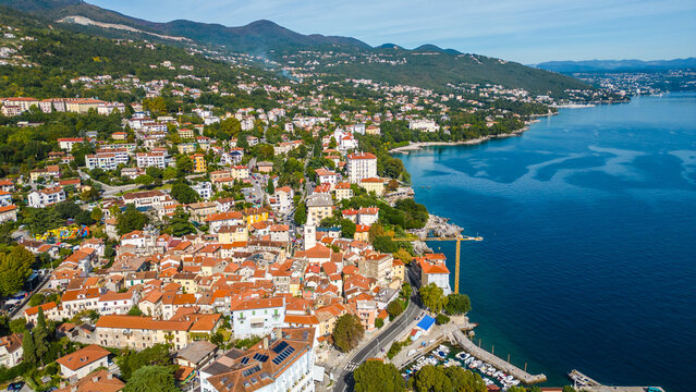Scenic aerial view of the coastal town Lovran on the Opatija Riviera, Croatia, with red-roofed houses, Adriatic Sea, and green Učka mountain slopes in the background