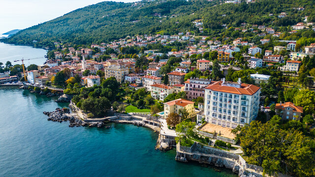 Aerial view of the Hotel Excelsior and the coastal promenade in Lovran, Croatia, surrounded by red-roofed houses, Adriatic Sea, and lush green hills of the Opatija Riviera