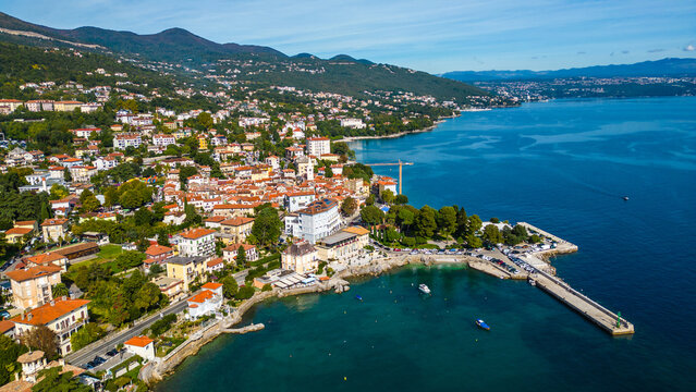 Scenic aerial view of the coastal town Lovran on the Opatija Riviera, Croatia, with red-roofed houses, Adriatic Sea, and green Učka mountain slopes in the background