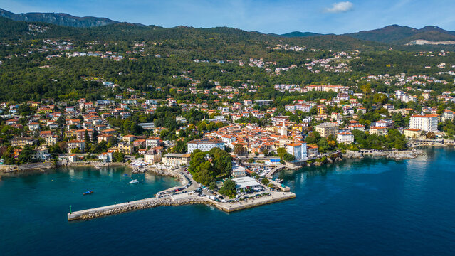 Scenic aerial view of the coastal town Lovran on the Opatija Riviera, Croatia, with red-roofed houses, Adriatic Sea, and green Učka mountain slopes in the background
