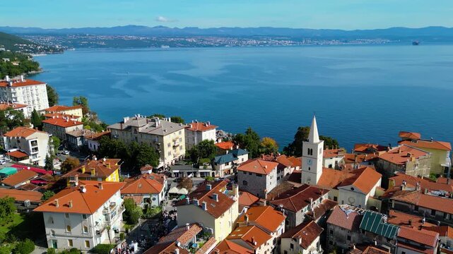 Scenic aerial view of the coastal town Lovran on the Opatija Riviera, Croatia, with red-roofed houses, Adriatic Sea, and green Učka mountain slopes in the background
