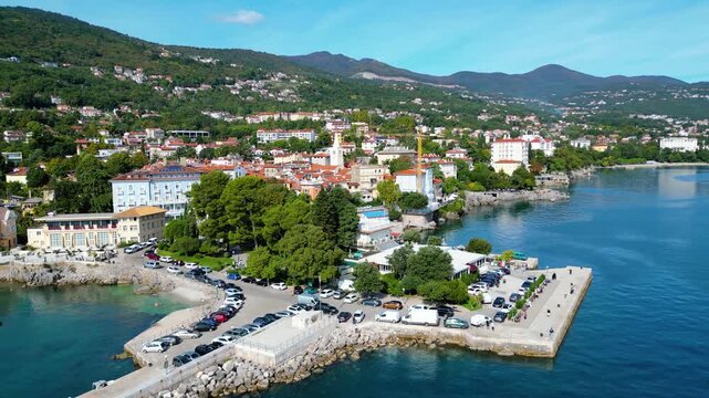 Scenic aerial view of the coastal town Lovran on the Opatija Riviera, Croatia, with red-roofed houses, Adriatic Sea, and green Učka mountain slopes in the background