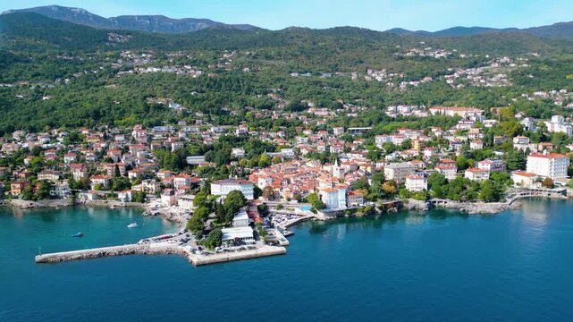 Scenic aerial view of the coastal town Lovran on the Opatija Riviera, Croatia, with red-roofed houses, Adriatic Sea, and green Učka mountain slopes in the background