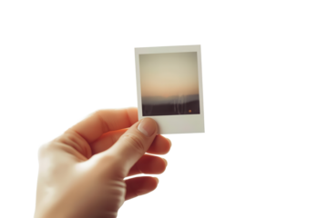 Hand holds a small photo, a memory captured in a tangible way, preserving a peaceful sunset scene.