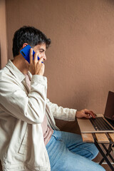 vertical Young Hispanic man teleworking, talking on phone and using laptop