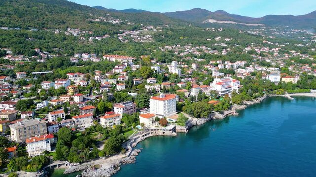 Aerial view of the Hotel Excelsior and the coastal promenade in Lovran, Croatia, surrounded by red-roofed houses, Adriatic Sea, and lush green hills of the Opatija Riviera