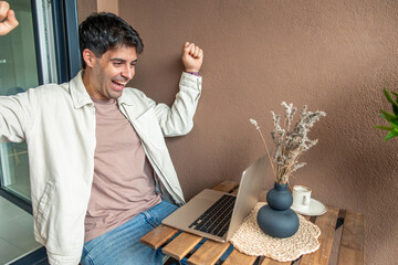 Young hispanic man celebrating remote work success at home