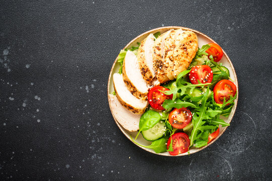Healthy food. Green salad with grilled chicken meat at black table. Top view.