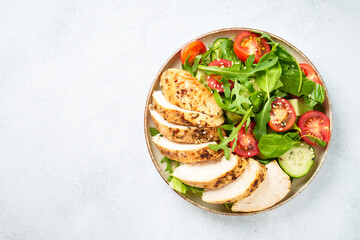 Chicken salad with grilled chicken breast and fresh vegetables at white kitchen table. Top view.