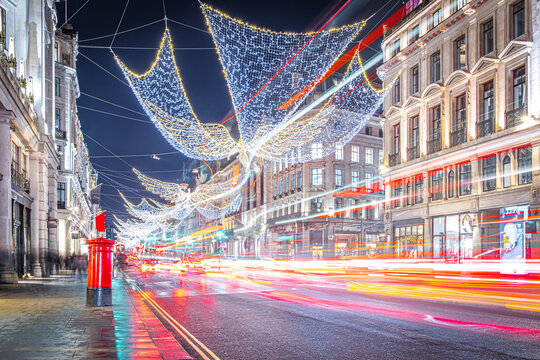 Classic London red bus navigates through a brightly lit street with Christmas decorations and busy foot traffic. Ideal for travel, holiday, or urban lifestyle themes.