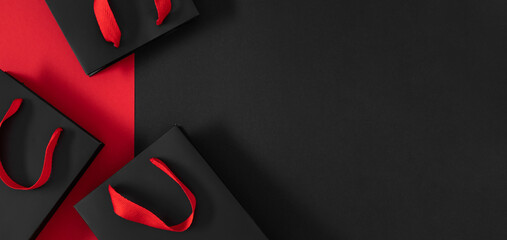 Minimalistic composition of black shopping bags with bright red handles on black and red background. Elegant contrast creates a luxurious and exclusive atmosphere, perfect for Black Friday banners.