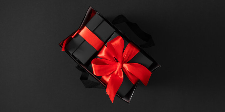 Black gift box with red ribbon on dark background. An elegant composition with a contrast of black and red is perfect for Black Friday sale banner