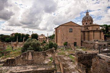 Ancient Roman ruins and historical buildings under dramatic cloudy sky in Rome