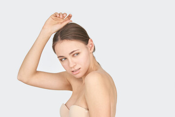 Obraz premium Young caucasian female posing with arm raised in neutral background, looking sideways with subtle smile.