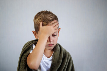 A child has a headache. The boy is holding his head in pain at home.
