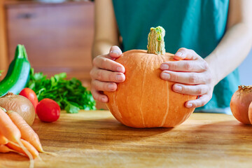 Female hands are holding an orange ripe large pumpkin, zucchini, carrots, tomatoes. Ripe autumn vegetables on a wooden table with space for a copy. Thanksgiving, Fall Holiday, Halloween