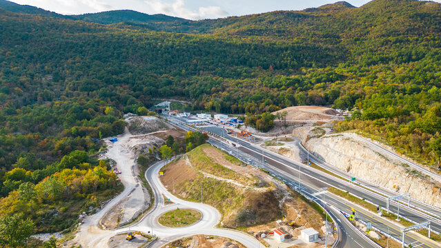 Aerial view of Učka (Ucka) Tunnel and toll booth surrounded on A8 motorway by autumn forest on the Rijeka side, showing colorful foliage and winding highway through the mountains