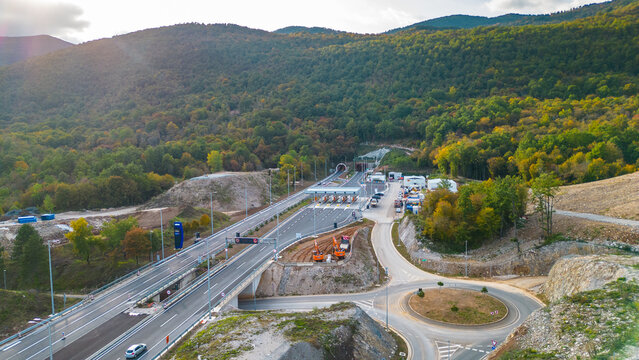 Aerial view of Učka (Ucka) Tunnel and toll booth surrounded on A8 motorway by autumn forest on the Rijeka side, showing colorful foliage and winding highway through the mountains