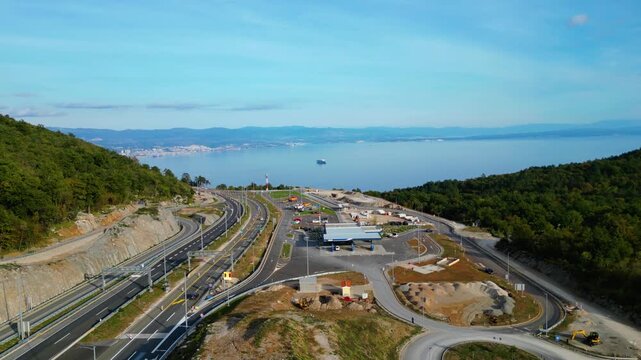 Aerial view of Učka (Ucka) Tunnel and toll booth surrounded on A8 motorway by autumn forest on the Rijeka side, showing colorful foliage and winding highway through the mountains