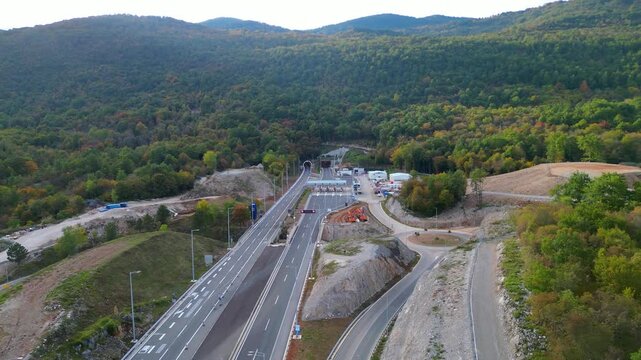 Aerial view of Učka (Ucka) Tunnel and toll booth surrounded on A8 motorway by autumn forest on the Rijeka side, showing colorful foliage and winding highway through the mountains