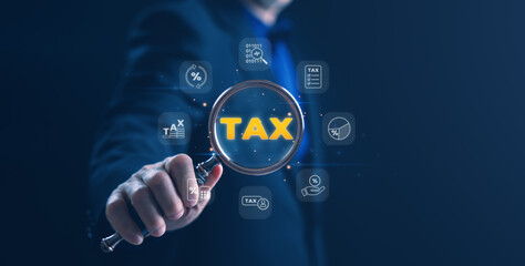 Businessman holding a magnifying glass with the word TAX surrounded by glowing white finance icons...